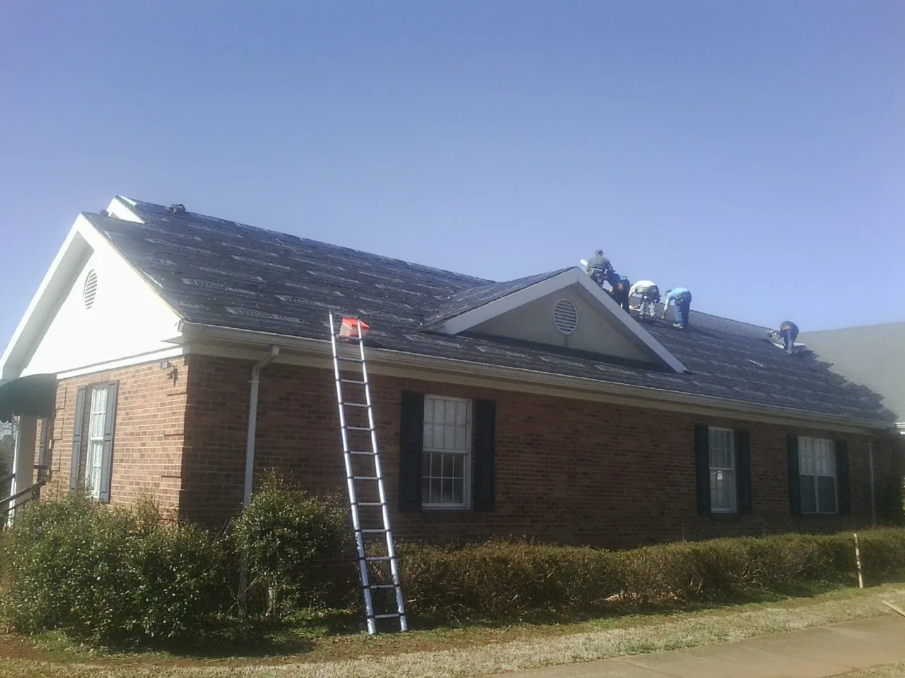 Crew tearing shingles off a brick ranch roof with a ladder set — Metal Roof Repair work by our crew in Huntington