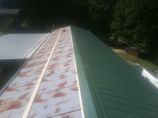 Old rusted panels beside newly installed green metal roofing — Wind Damage Roof Repair by Roofing Brothers in Huntington