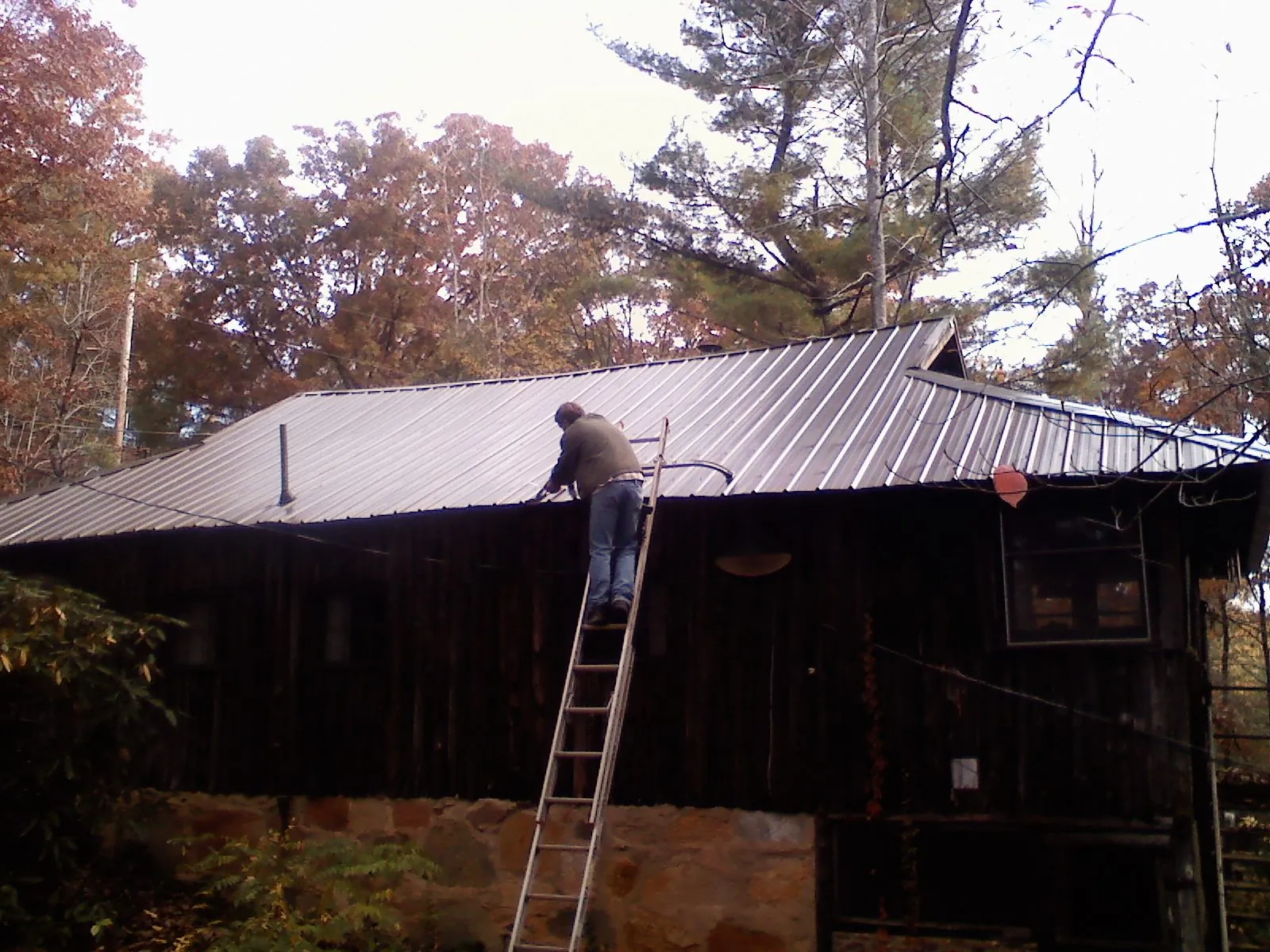 Roofer on a ladder working along the edge of a cabin metal roof in Huntington